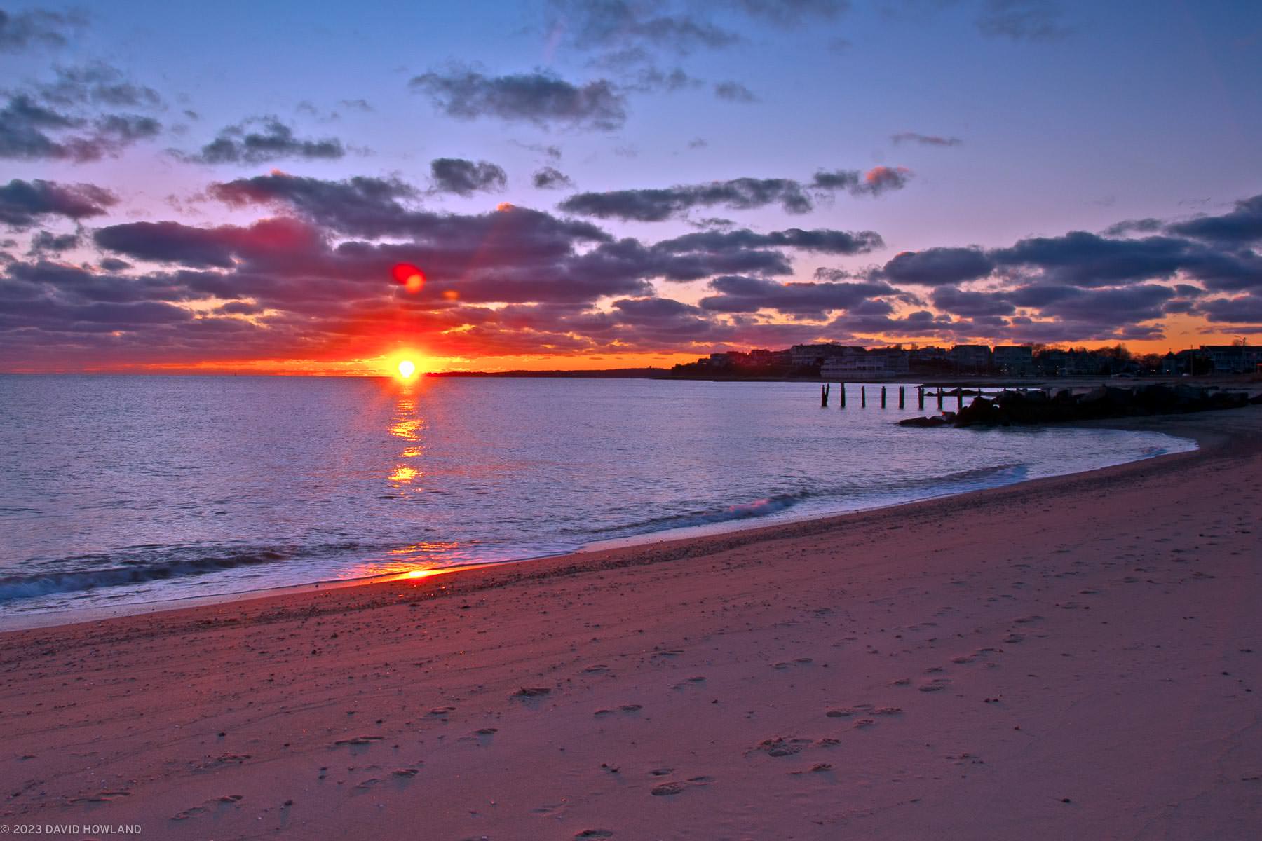 A photo of a purple and orange sunset over the waters of Vineyard Sound and Nobska Lighthouse in Falmouth, Massachusetts on Cape Cod