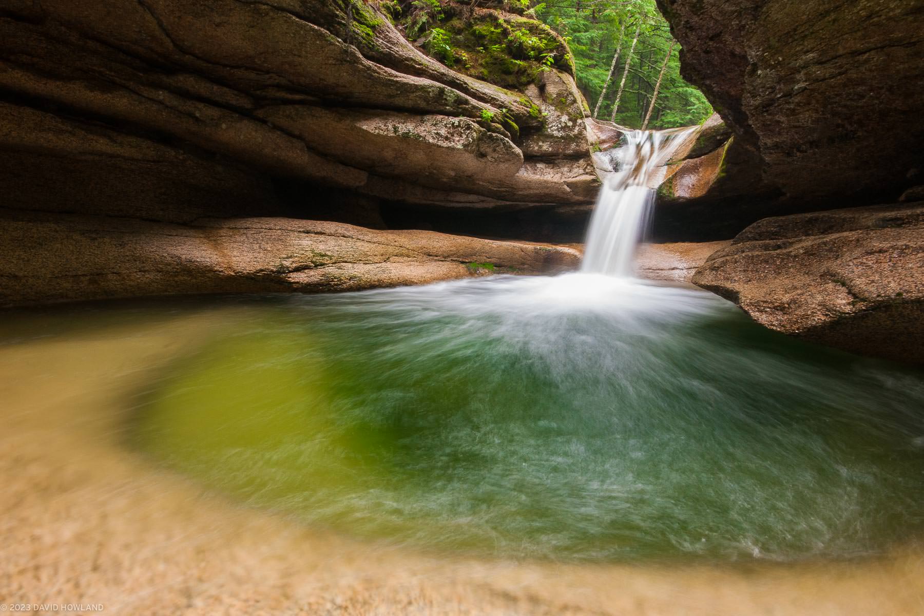 A photo of a waterfall cascading into a deep granite cavern in the White Mountain National Forest of New Hampshire.